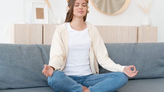 Calm young woman sitting on couch, practicing meditation yoga with mudra hands